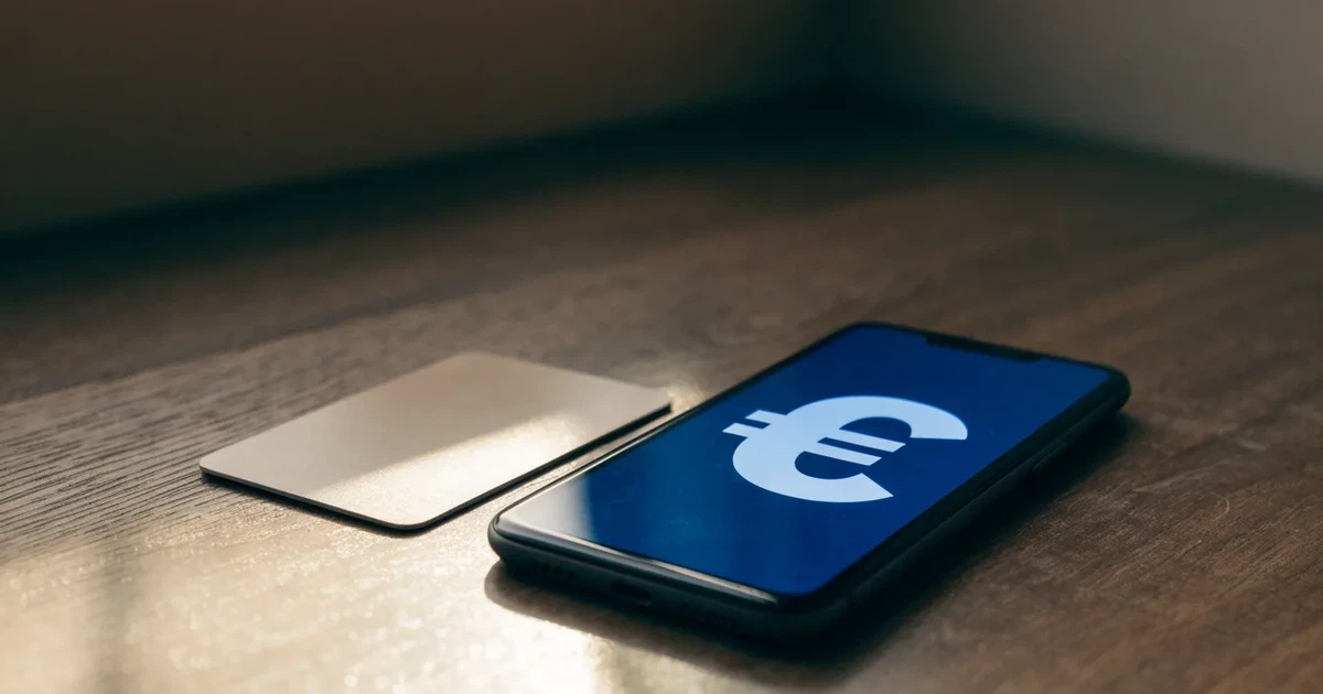 Uno smartphone e una carta di pagamento affiancati su un tavolo di legno, con alcune banconote da euro accanto